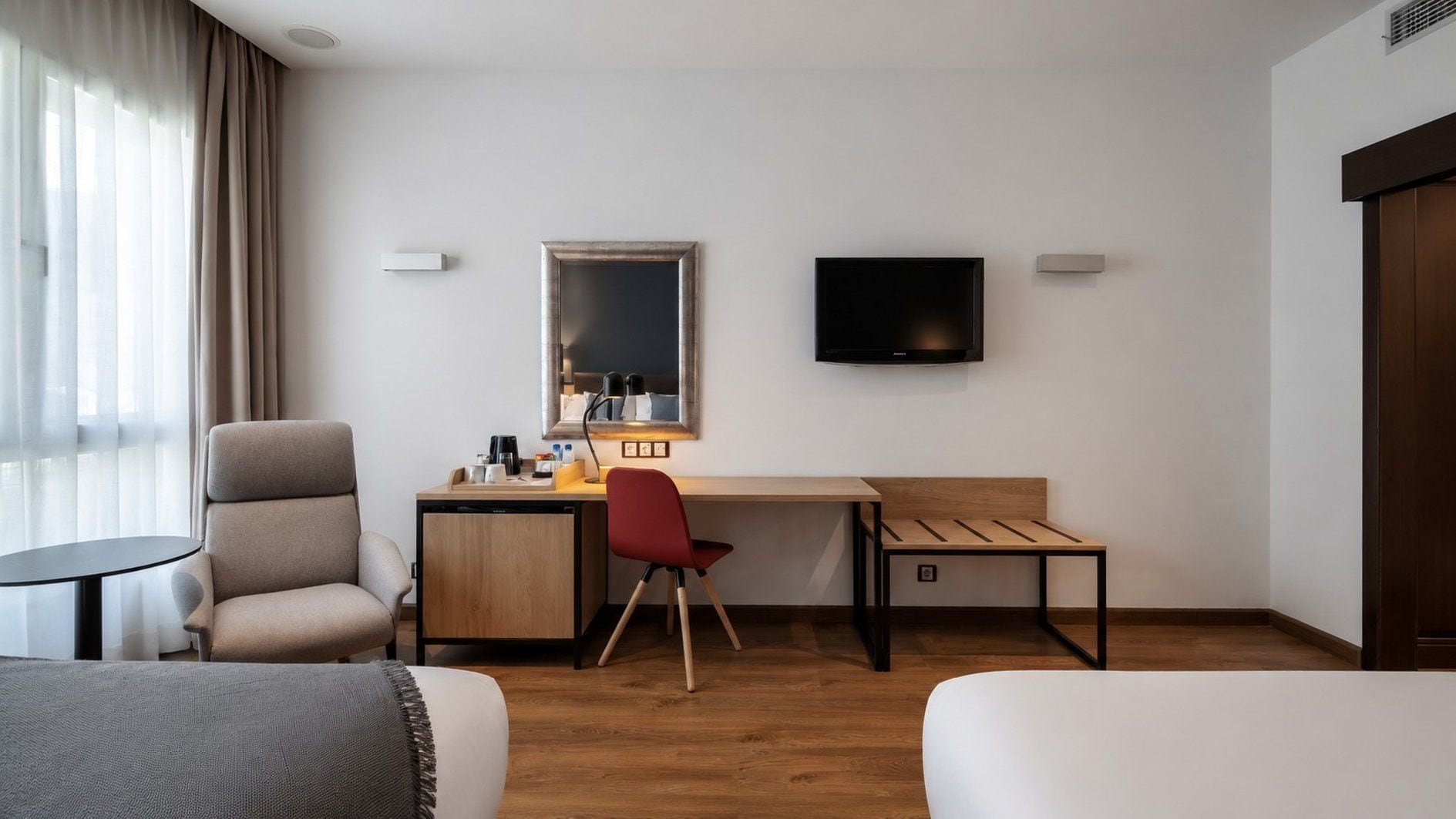 Ein Hotelzimmer mit Bett, Schreibtisch, Stuhl, Fernseher und einem Fenster mit Vorhängen.