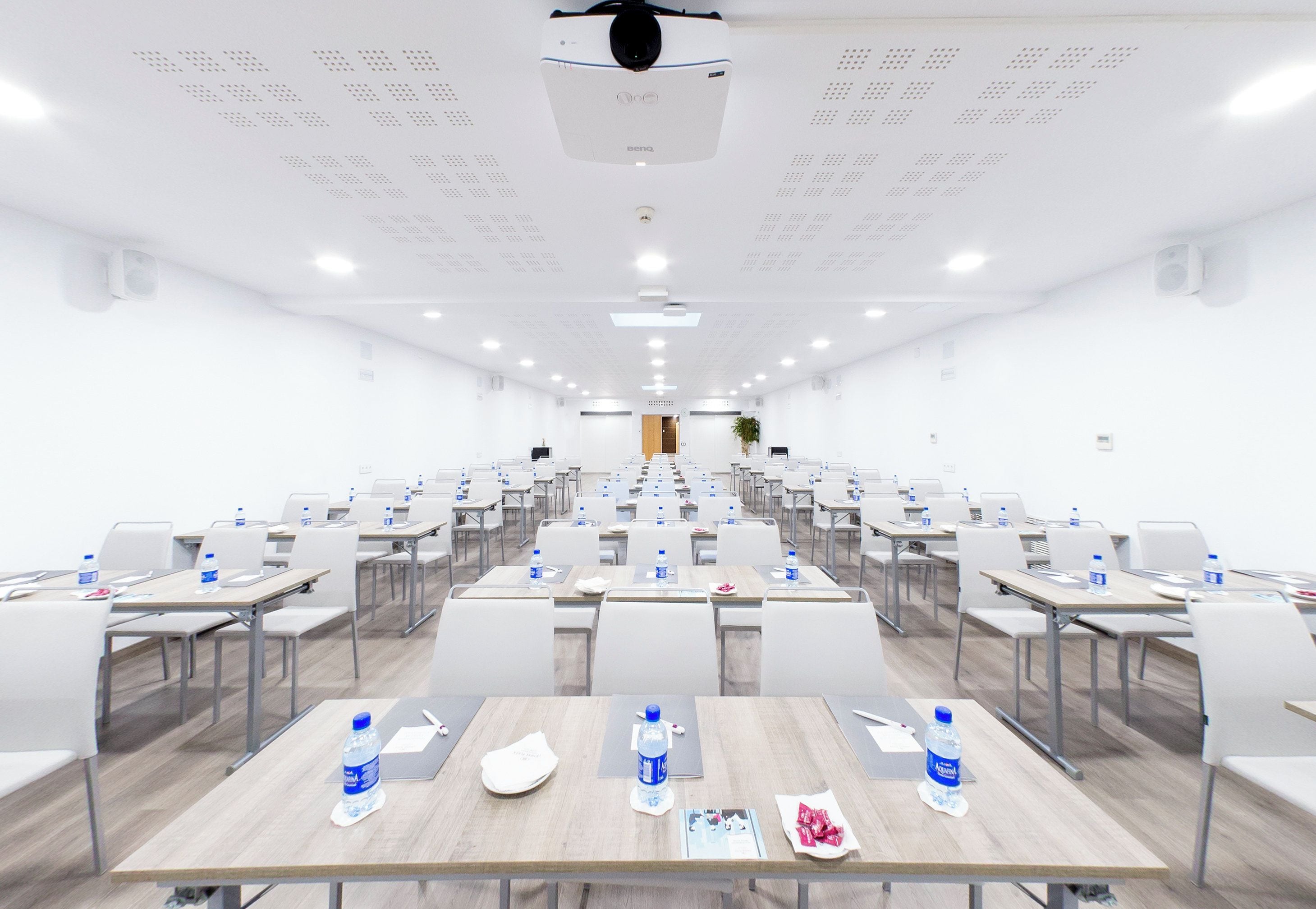 Uma sala de conferências com mesas, cadeiras e garrafas de água dispostas em fileiras.
