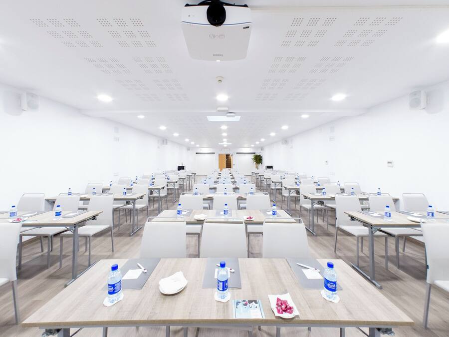 Un salón de conferencias con mesas dispuestas en filas, sillas y botellas de agua.
