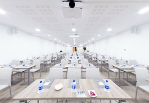 Un salón de conferencias con mesas dispuestas en filas, sillas y botellas de agua.