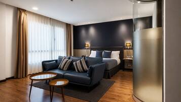 Habitación de hotel moderna con una cama de tablero cabecera azul oscuro, un sofá de cuero, dos pequeñas mesas de madera y un gran pilar cilíndrico.