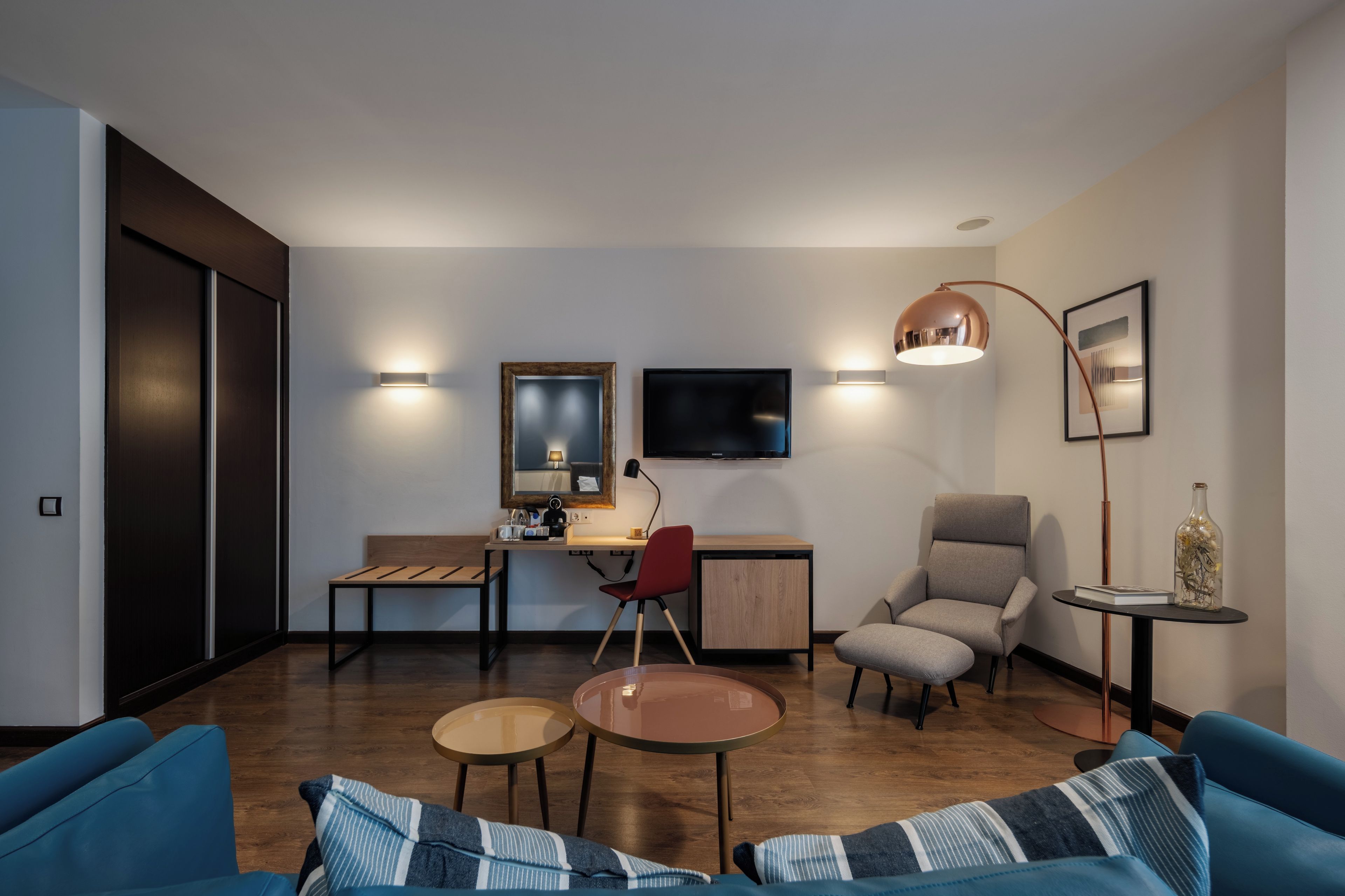 Una sala de estar moderna con sofá, mesa de centro y sillones. Incluye un escritorio con silla, televisor e iluminación instalada en la pared.