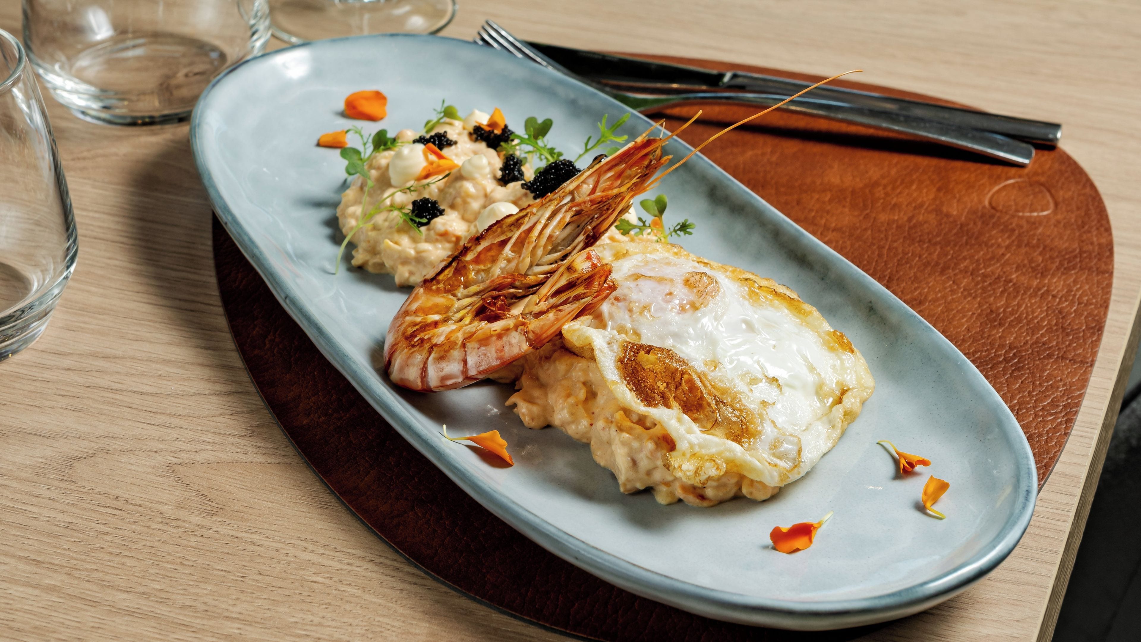 A plate with a grilled shrimp, a fried egg, and a creamy side dish, possibly rice, on a blue plate.