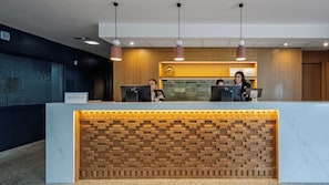 Un comptoir d’accueil avec deux employés, un mur décoré en bois et un plan de travail en marbre.