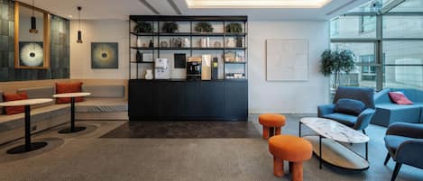 A modern lounge area with seating, a coffee station, and a bookshelf.