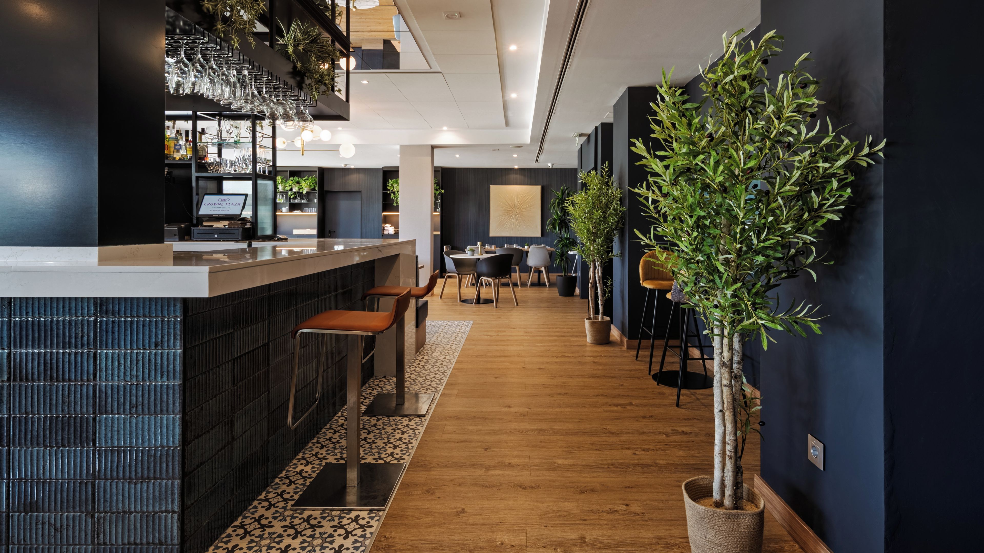 Zona de bar moderna con mostrador, taburetes y plantas en macetas.
