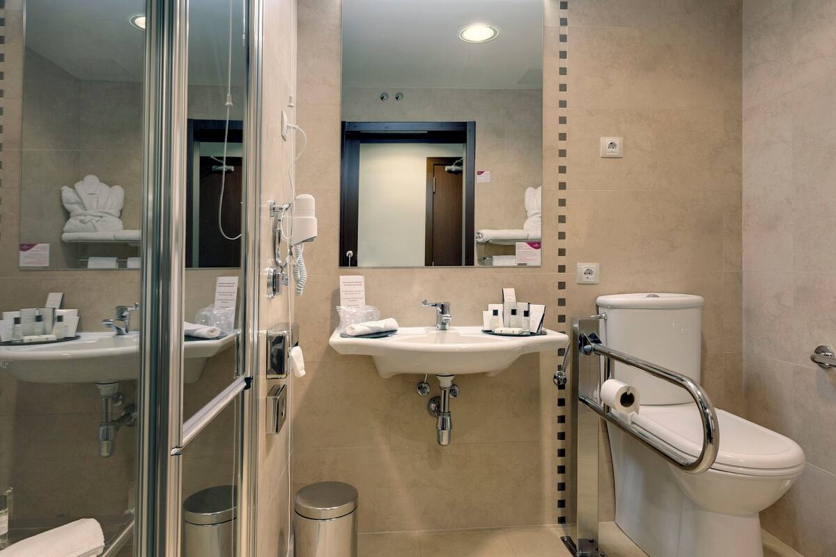 Un baño moderno con ducha de vidrio, dos lavamanos, un inodoro y un secador de manos.