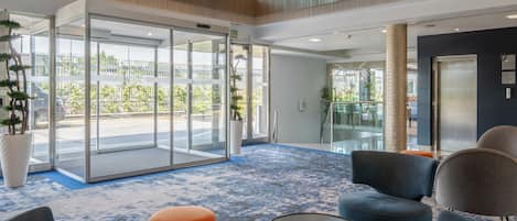 A modern lobby with a glass door entrance, seating area, and a blue patterned carpet.