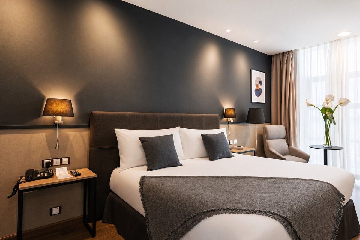 A hotel room with a large bed, bedside lamps, a chair, a small table, and a vase with flowers.