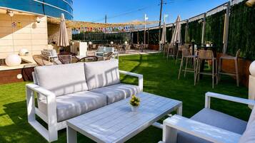 An outdoor seating area with a sofa, table, and chairs, surrounded by a green lawn and a building with a blue facade.