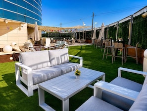 Un espace extérieur aménagé avec un canapé, une table et des chaises, entouré d’une pelouse verdoyante et d’un bâtiment à la façade bleue.