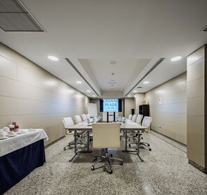 Une salle de conférence équipée d’une longue table, de chaises et d’un écran numérique affichant le texte : « CROWNE PLAZA BY IHG, aéroport de Madrid ».