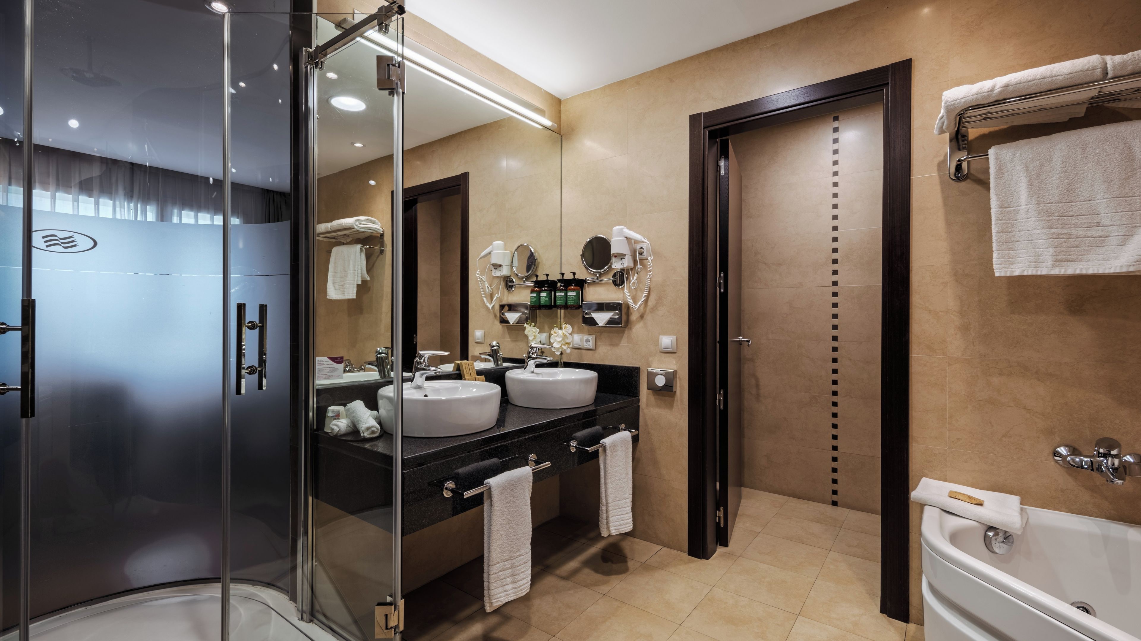 A modern bathroom with a glass shower enclosure, dual sinks, a large mirror, and a bathtub.