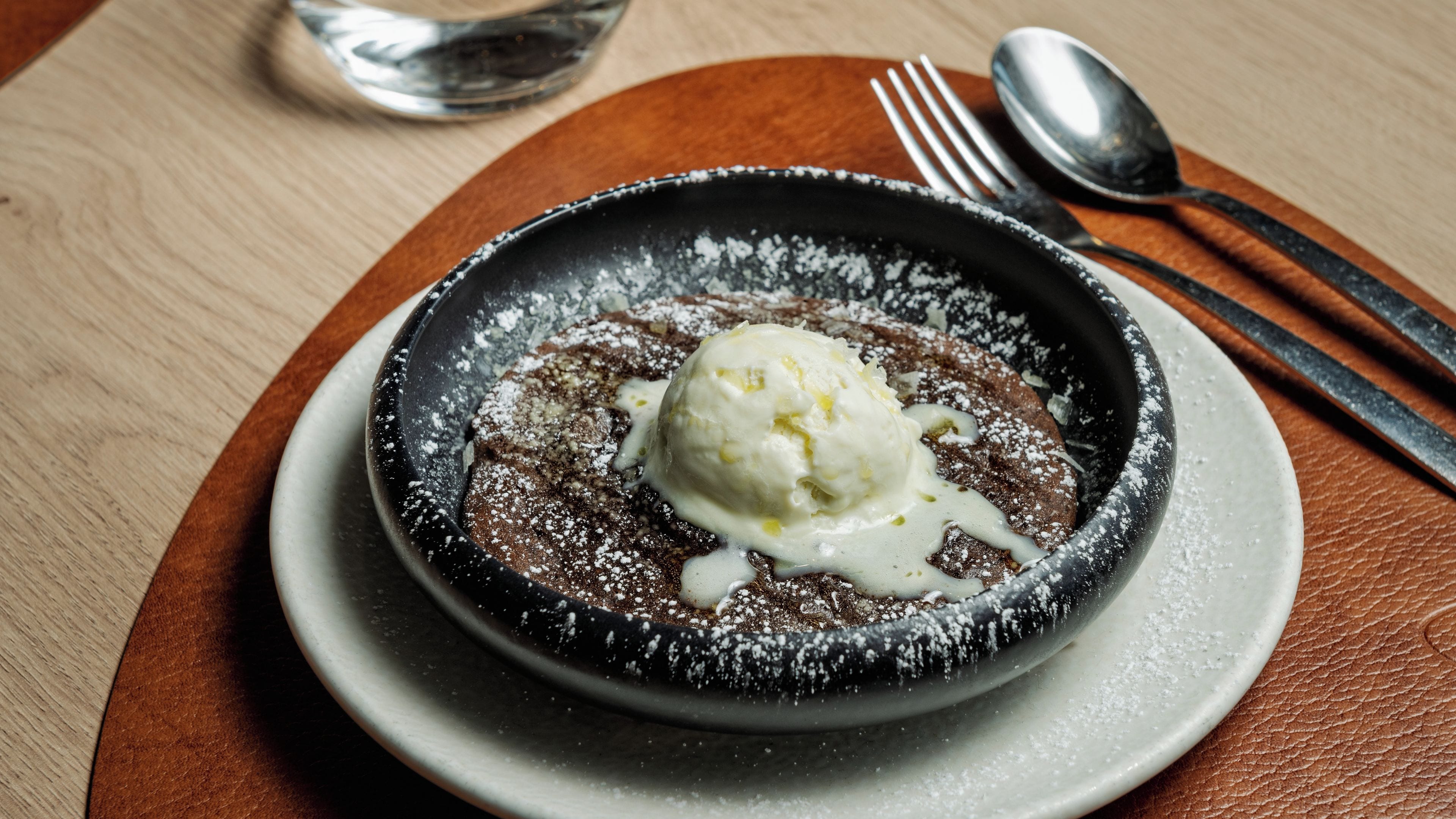 A dessert in a bowl on a plate, with a spoon and fork beside it.