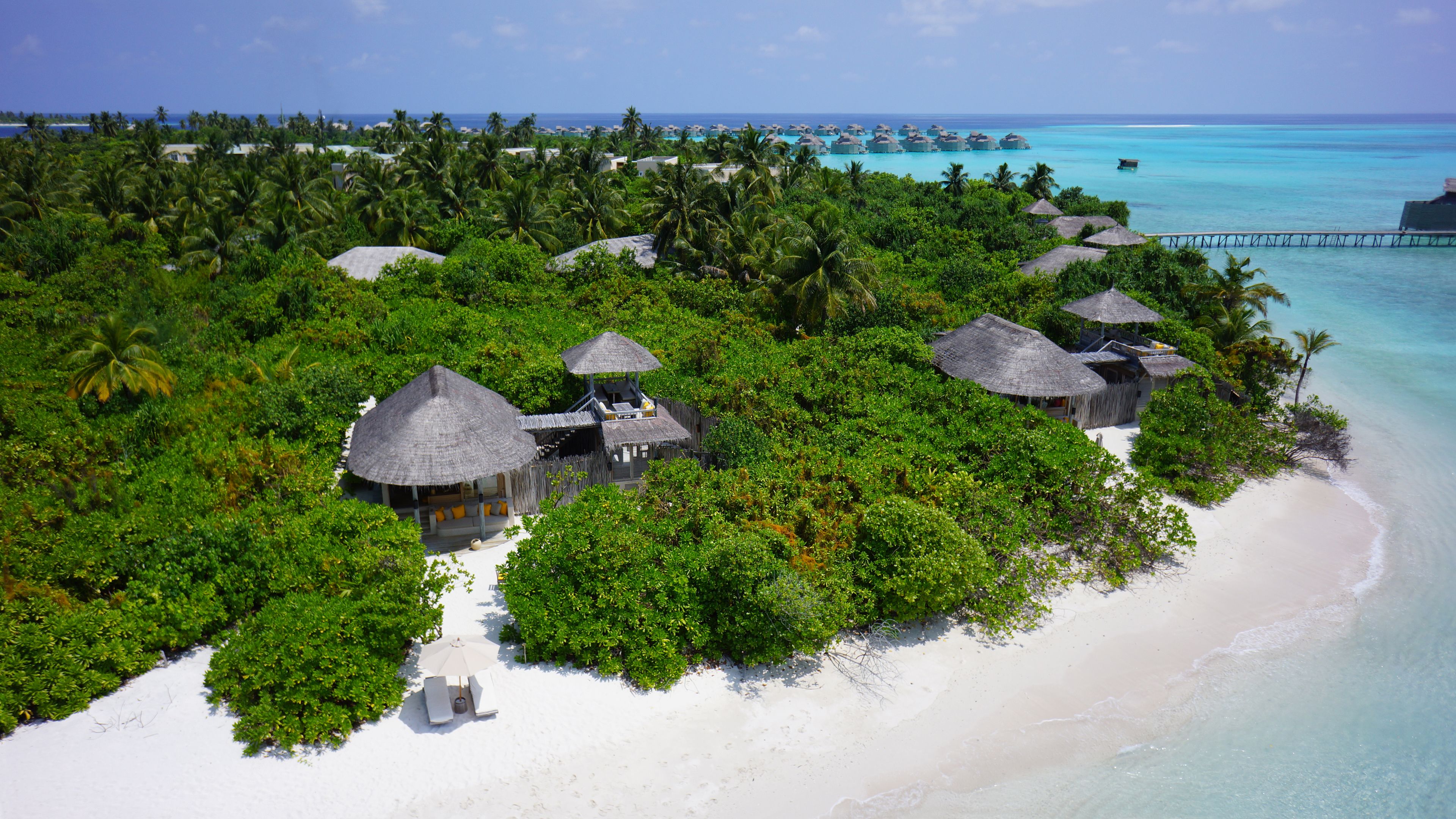 An aerial view of a tropical resort with overwater bungalows surrounded by lush greenery and a pristine beach.