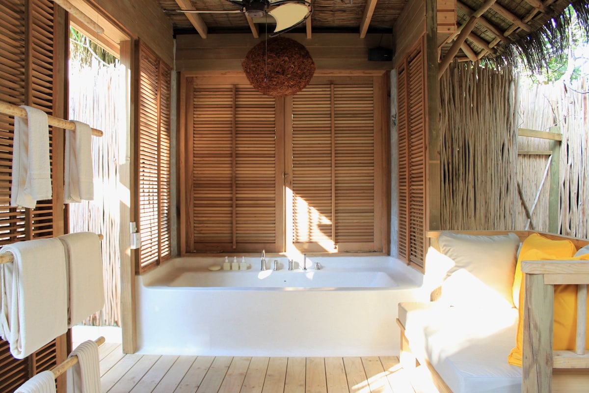 A wooden room with a large bathtub, wooden shutters, and a hanging light fixture.