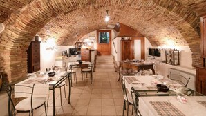 An arched brick ceiling in a dining area with tables and chairs, a staircase leading to an upper level, and a wooden cabinet. - Locanda Alfieri (Termoli)