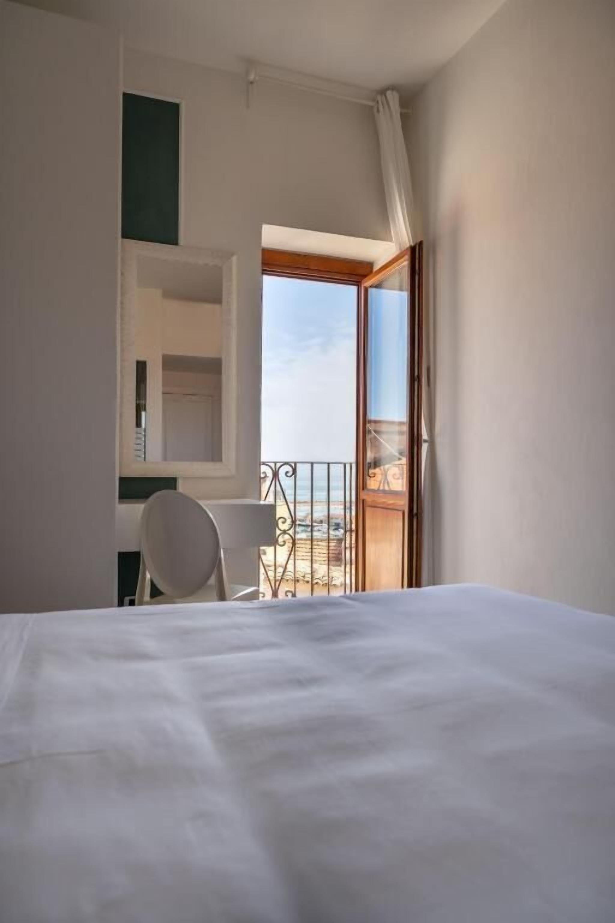 Una camera d'albergo con un letto, una sedia, un tavolino e un balcone vista spiaggia.