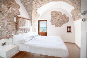 A bedroom with a stone wall, a bed, a nightstand, and a view of the sea through an open door. - Locanda Alfieri (Termoli)