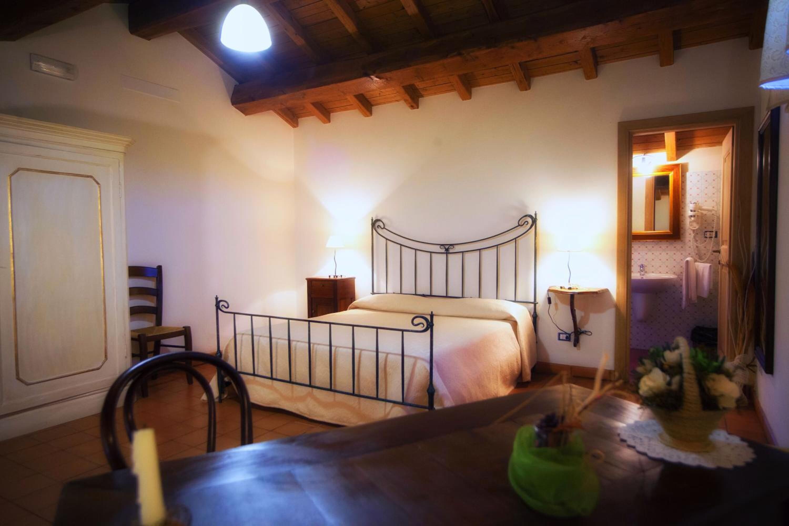 Ein Schlafzimmer mit Holzbalkendecke, Metallbettgestell, Nachttisch, Stuhl und einem Beistelltisch.