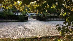 Ein Pflasterweg führt zu einem eingezäunten Bereich mit Bänken und Bäumen.