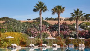 A pool with lounge chairs and umbrellas, surrounded by palm trees and flowering plants. - VOI Marsa Siclà Essentia (Scicli)