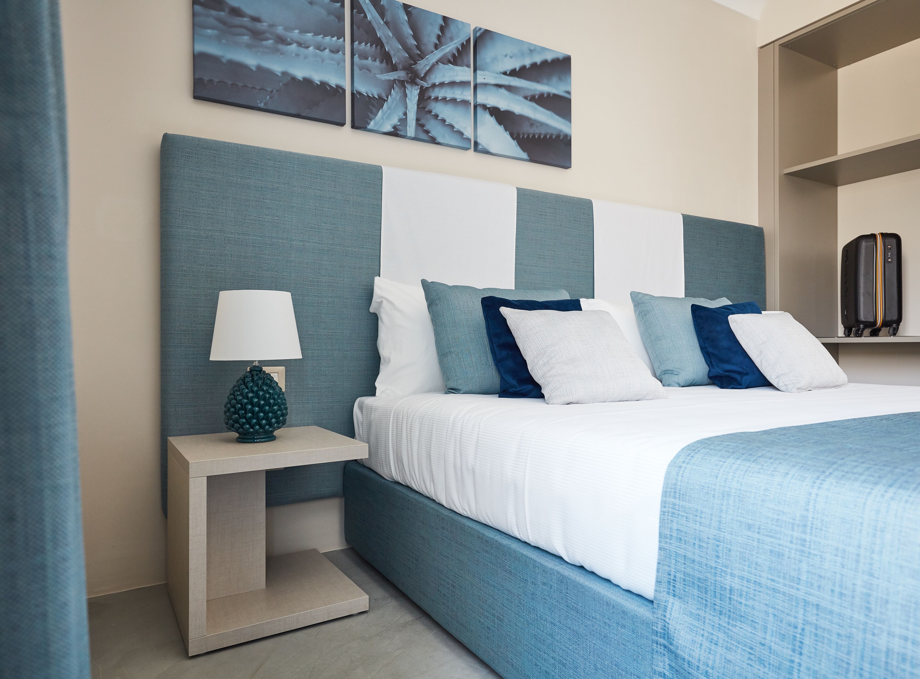 Una camera d'albergo moderna con un letto grande, un comodino con una lampada e opere d'arte alle pareti.