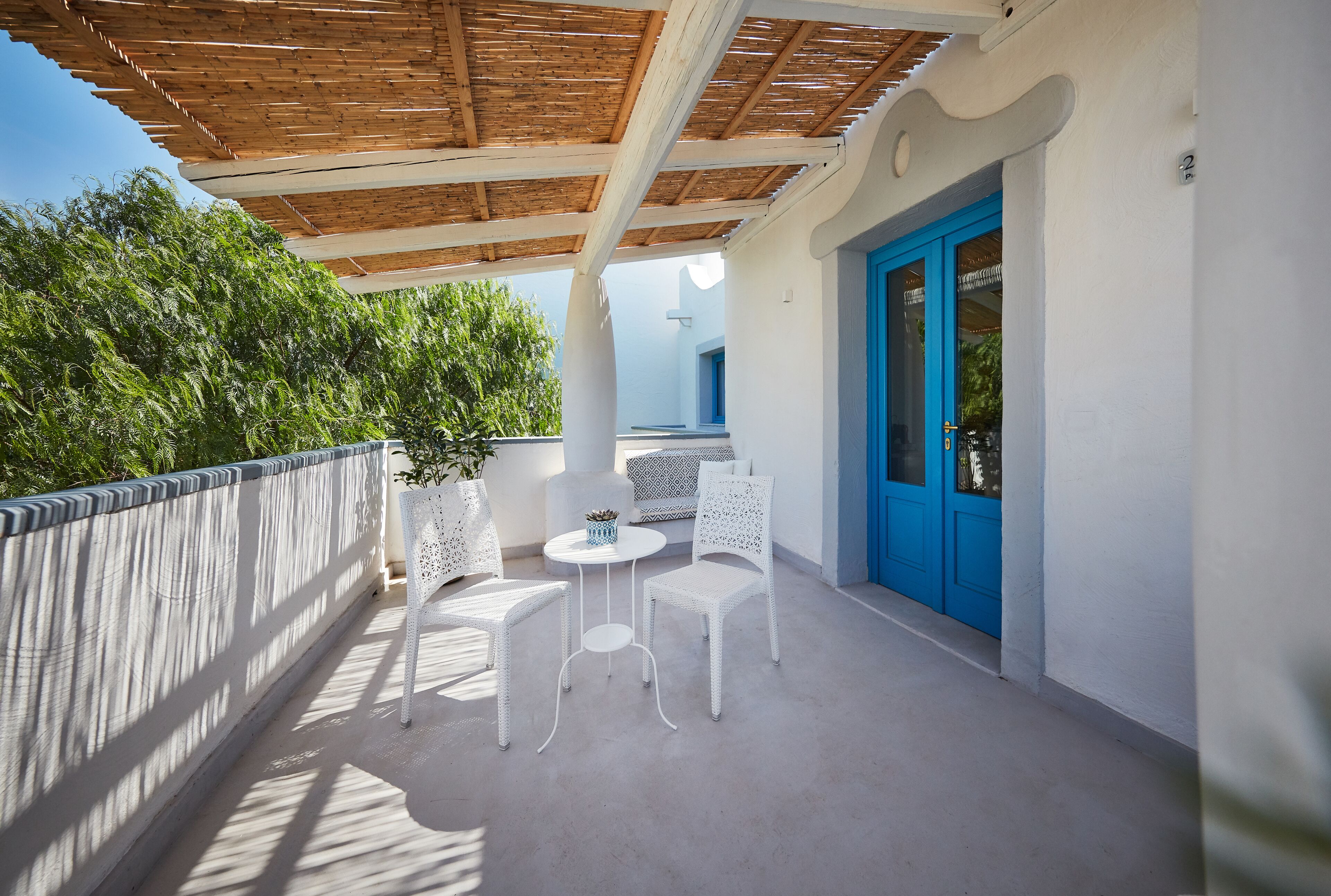 A balcony with white wicker furniture, a blue door, and a wooden ceiling.