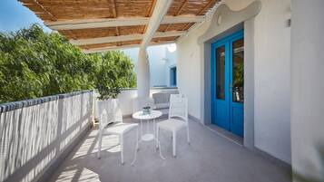 A balcony with white wicker furniture, a blue door, and a wooden ceiling.