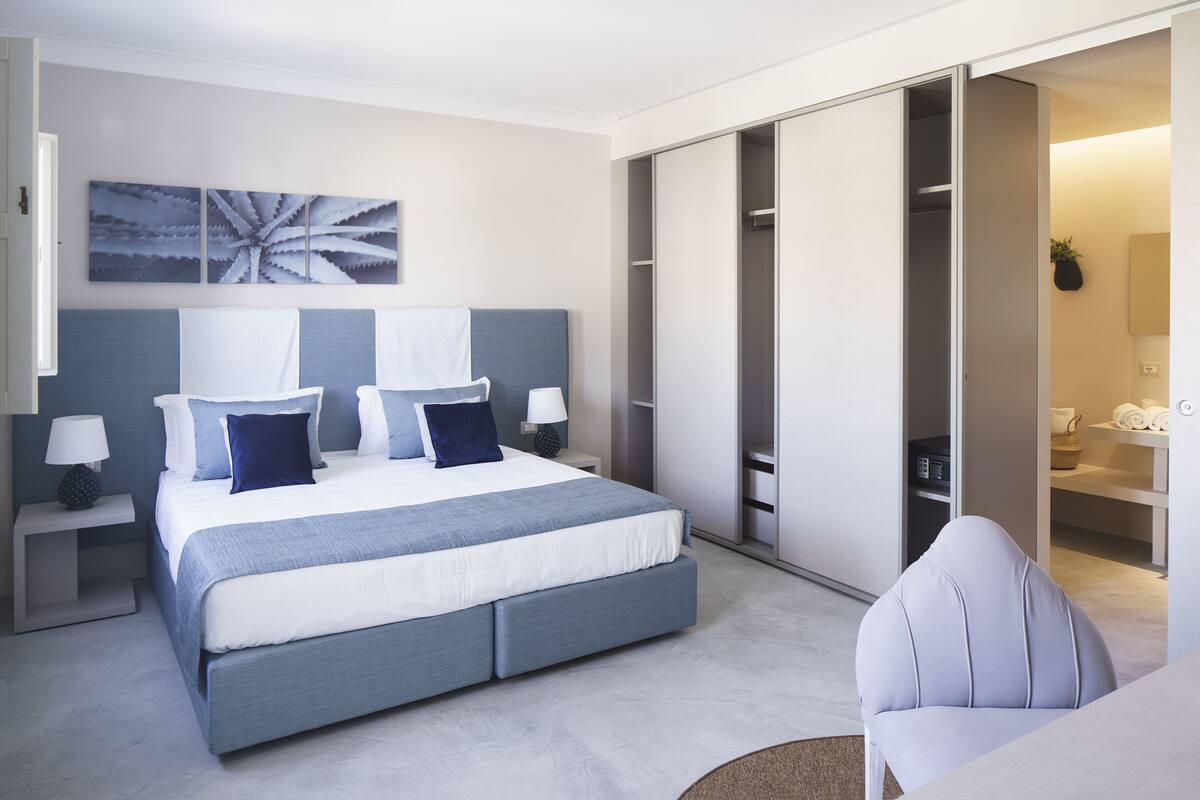A modern bedroom with a large bed, a wardrobe, and a seating area.