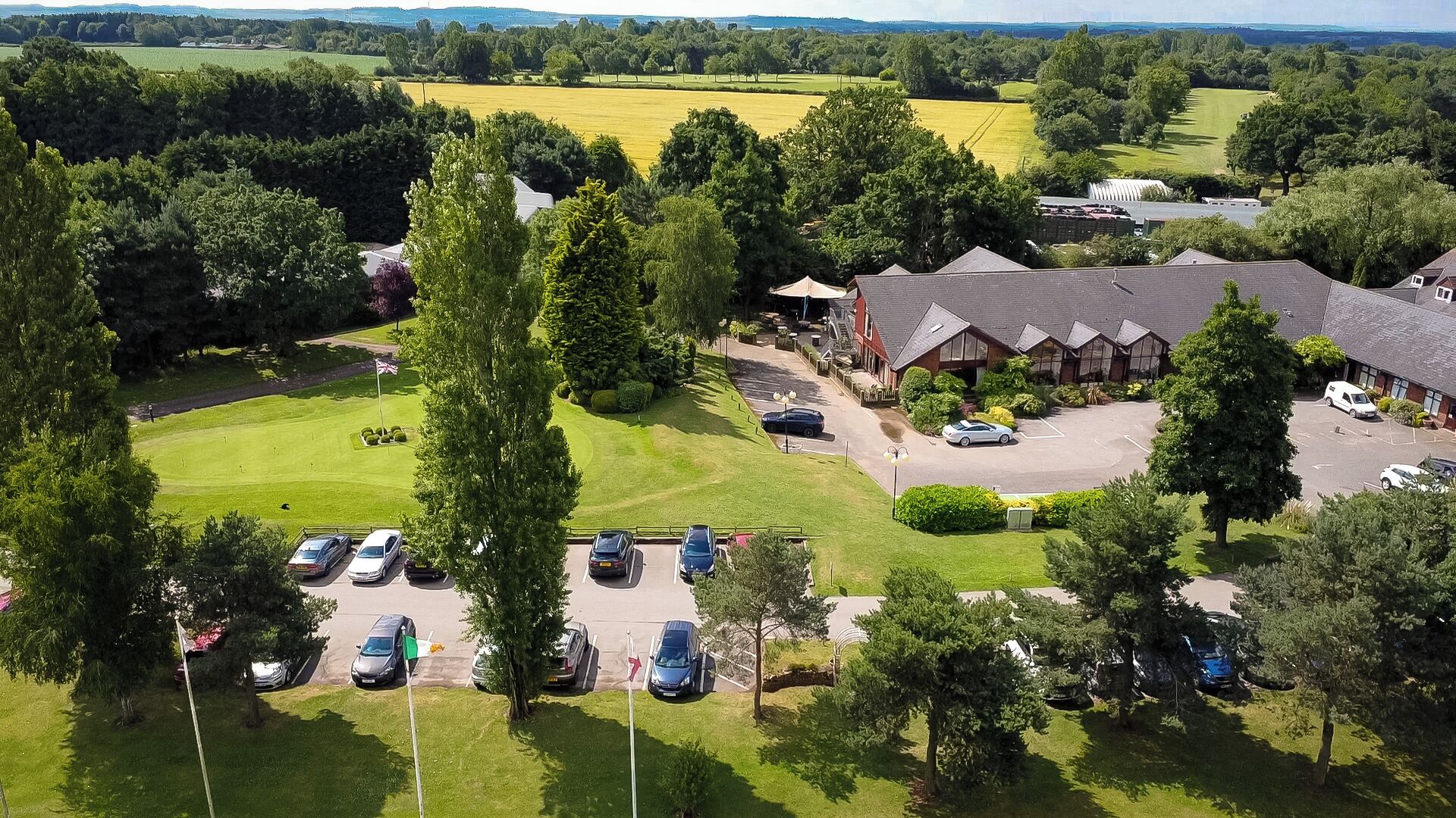 Luftaufnahme eines Hotels mit mehreren Parkplätzen, einem Golfplatz und umliegender Bepflanzung.