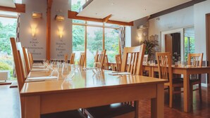 A dining area with wooden tables and chairs, large windows, and wall-mounted lights. - Draycote Hotel and Whitefields Golf Club (Rugby)