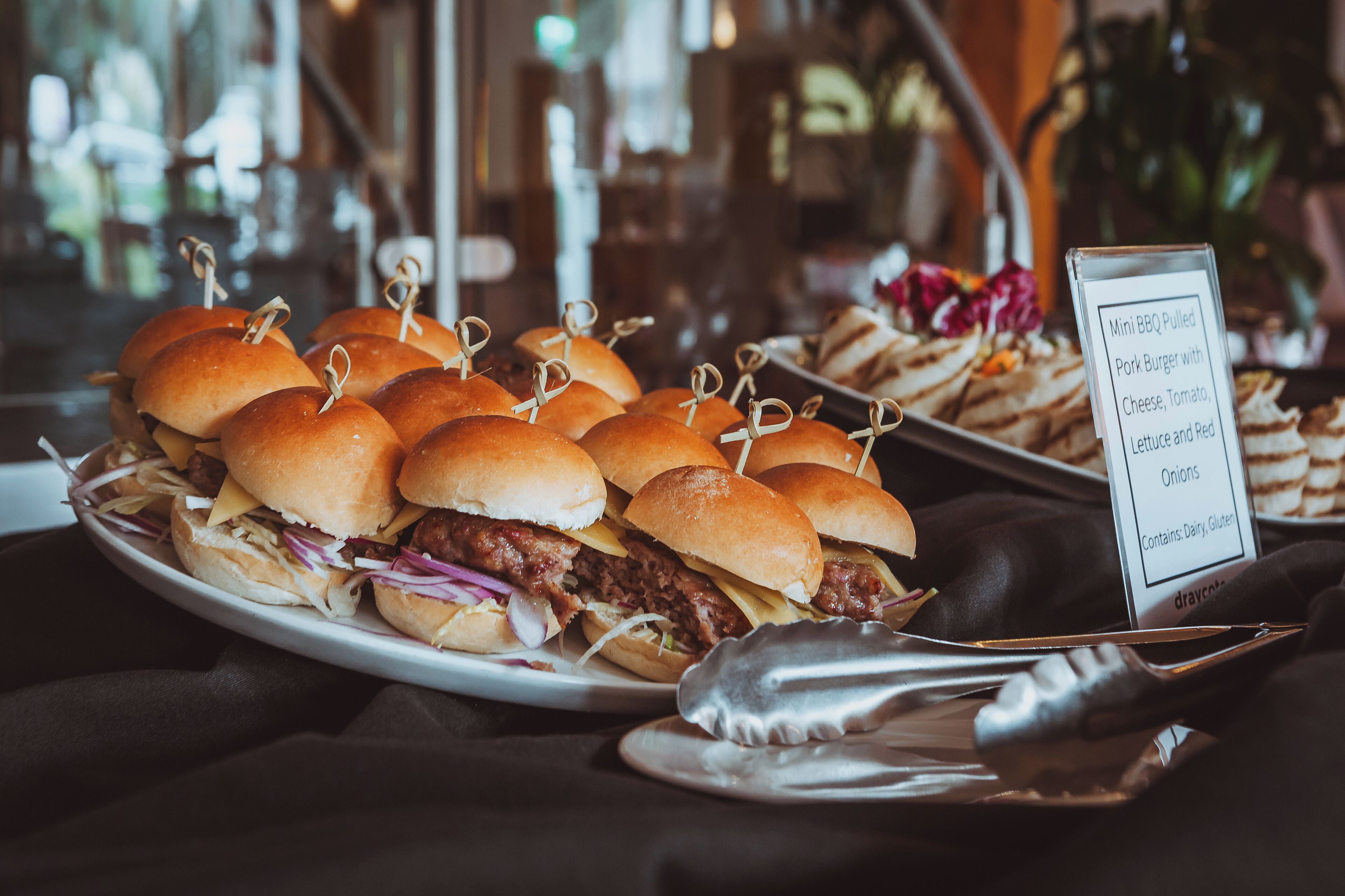 Un plato de mini hamburguesas de cerdo desmenuzado a la barbacoa, con panecillos, queso, tomate, lechuga y cebollas rojas.
