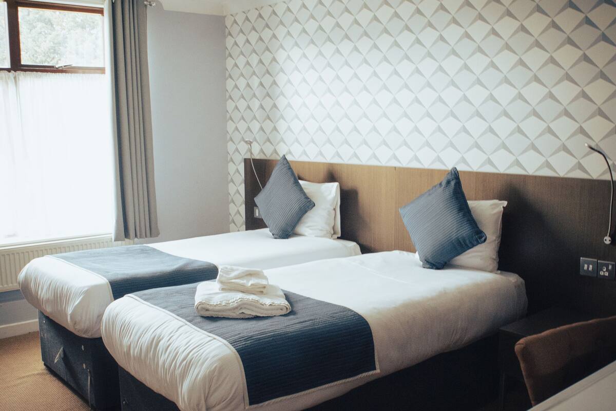 A hotel room with two beds, a desk, and a window with curtains.