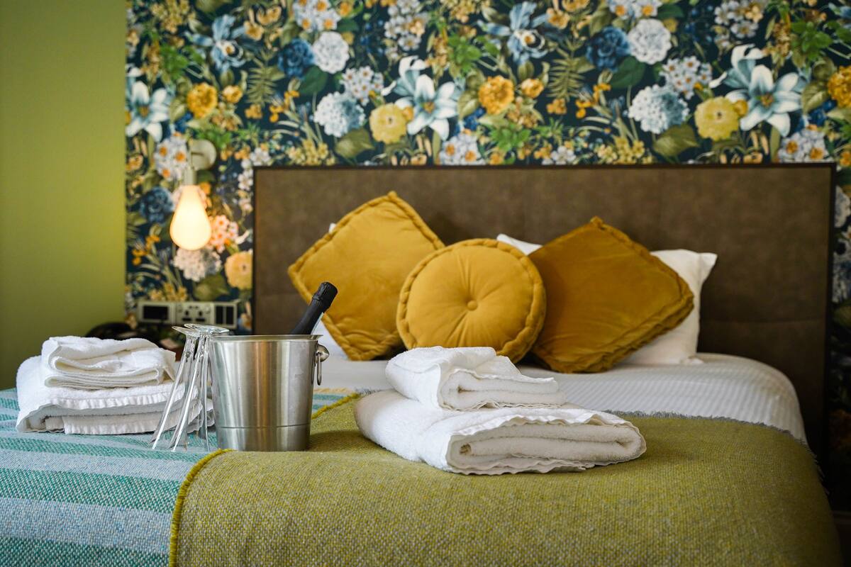 A neatly made bed with white linens, a metal container, and a green throw blanket.