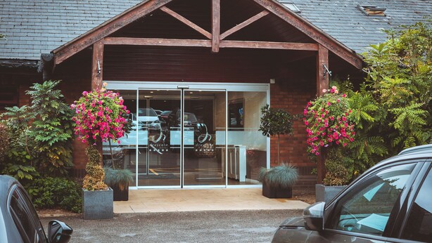 A building with a wooden gable roof, large glass doors, and potted plants with pink flowers. - Draycote Hotel and Whitefields Golf Club (Rugby)