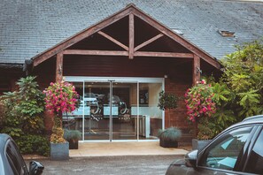 A building with a wooden gable roof, large glass doors, and potted plants with pink flowers. - Draycote Hotel and Whitefields Golf Club (Rugby)