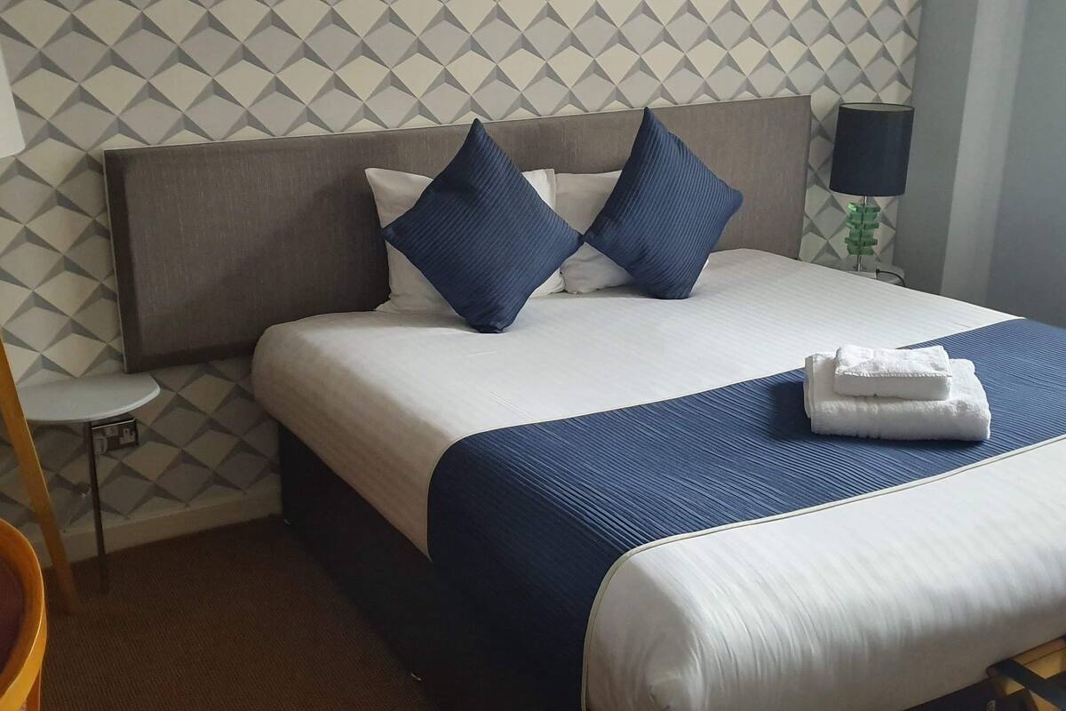 A hotel room with a bed, a nightstand, a lamp, and a chair.