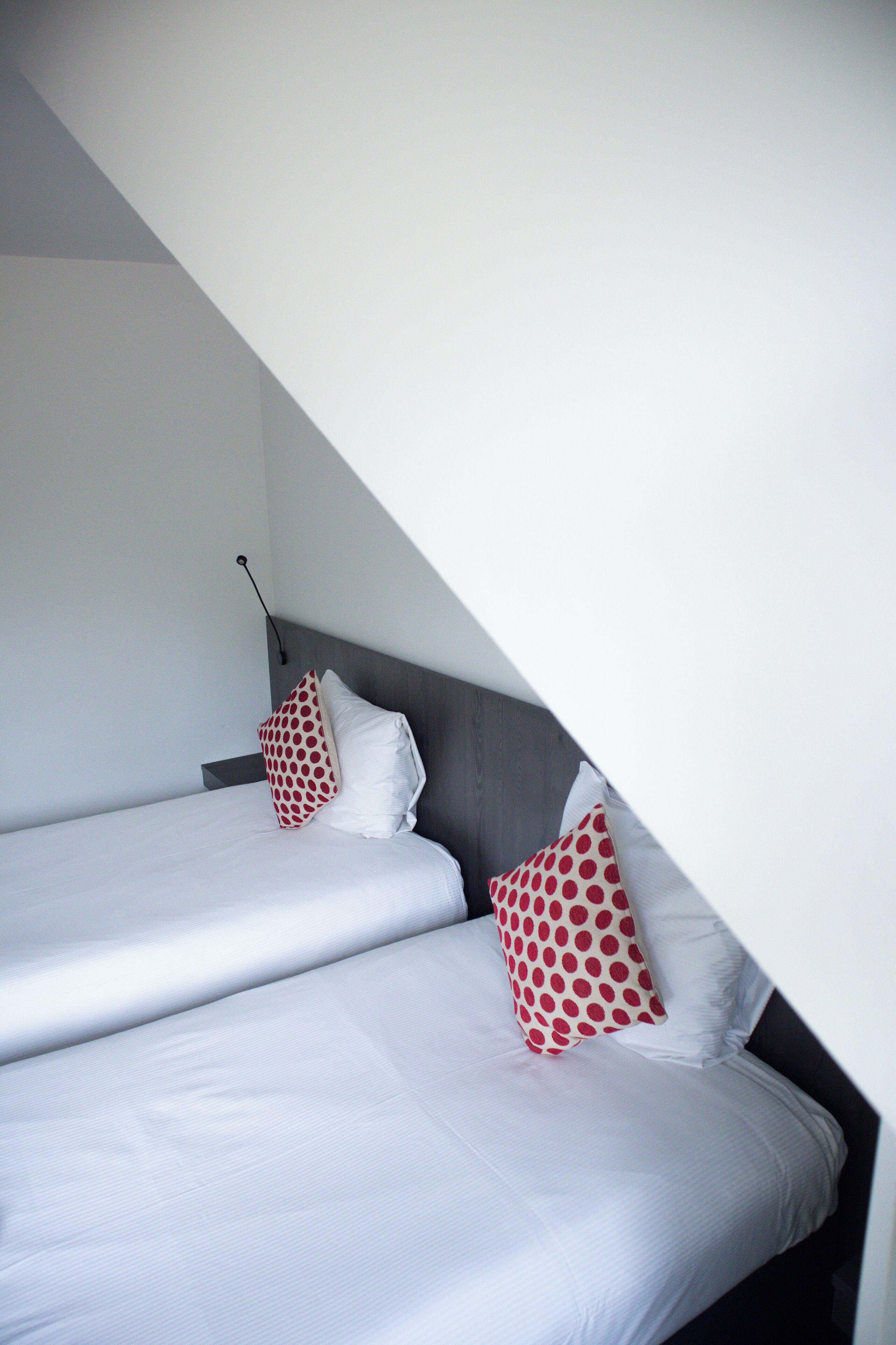 Habitación de hotel con dos camas, cada una con ropa blanca y almohadones de lunares rojos.