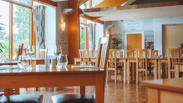 A restaurant with wooden tables and chairs, large windows, and a wall with a quote about food.