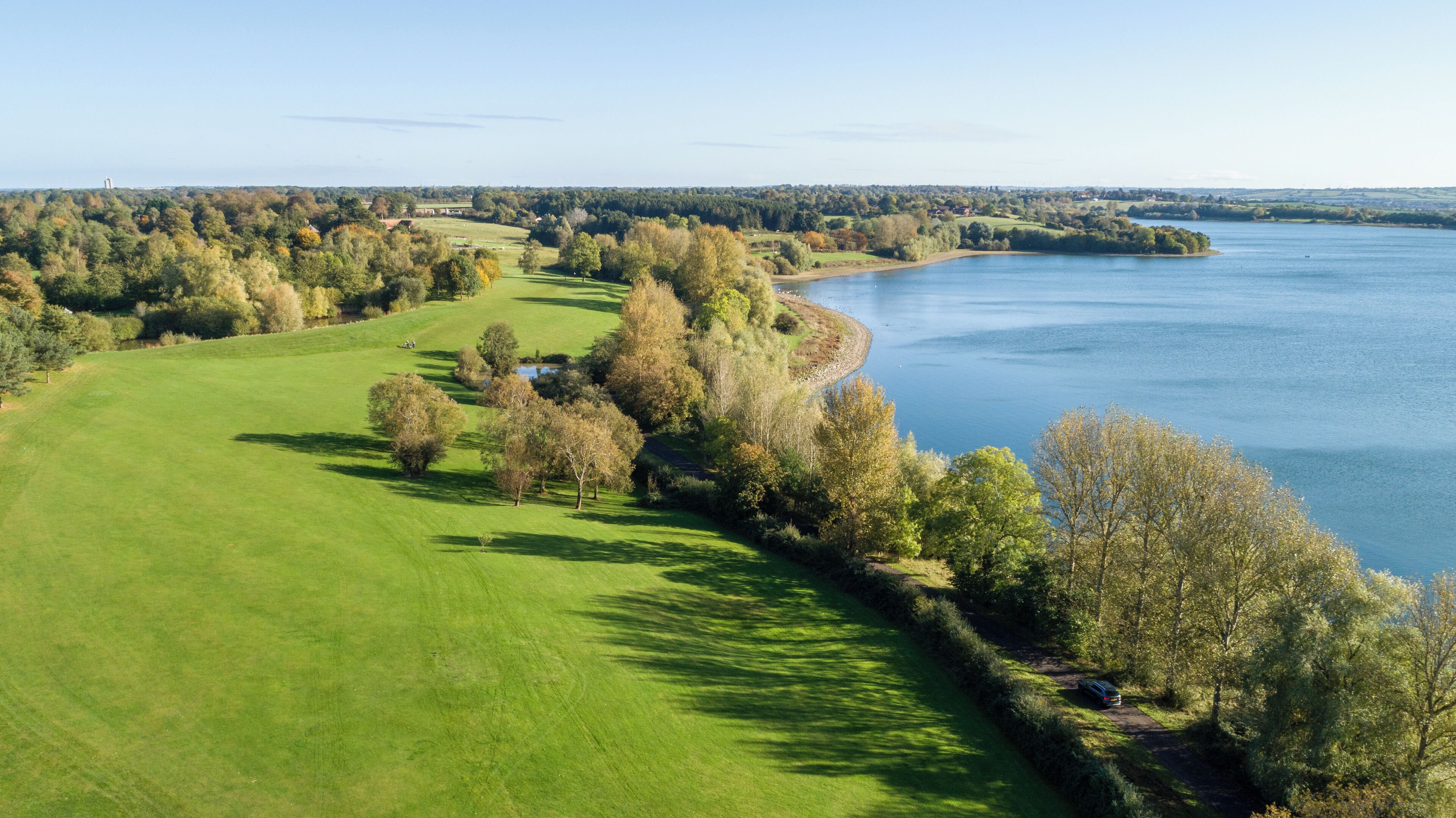 Campo de golf con un lago, rodeado de árboles y un cielo despejado.