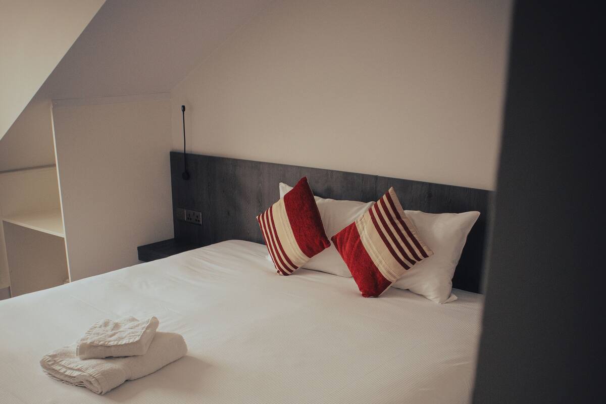 A neatly made bed with white linens and striped pillows, a bedside table, and a modern headboard.