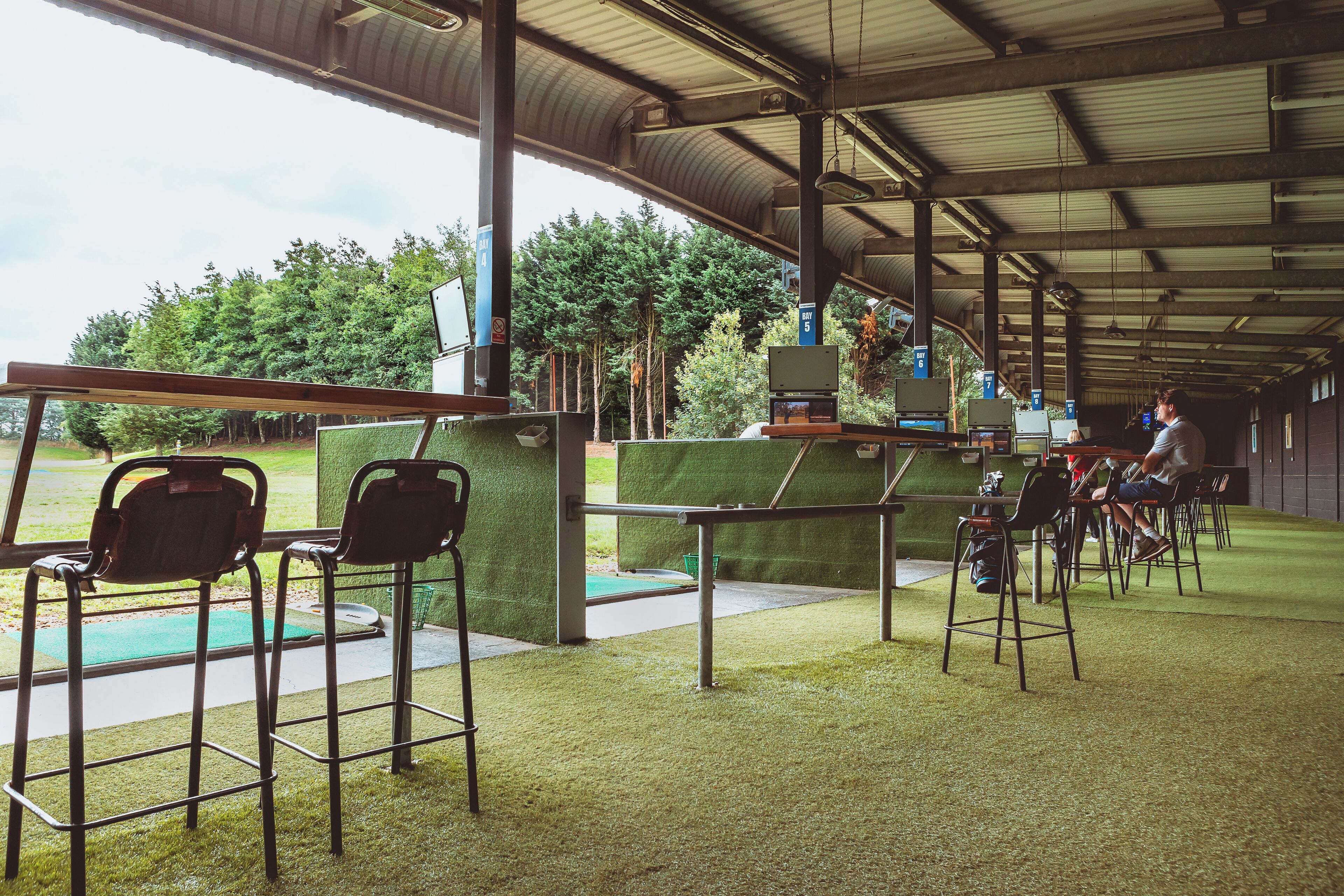 Un espace intérieur doté d’un revêtement de sol en gazon synthétique, de chaises en métal et d’un comptoir avec un ordinateur.