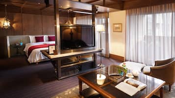 A hotel room with a bed, a TV, a coffee table, a chair, and a window with curtains.