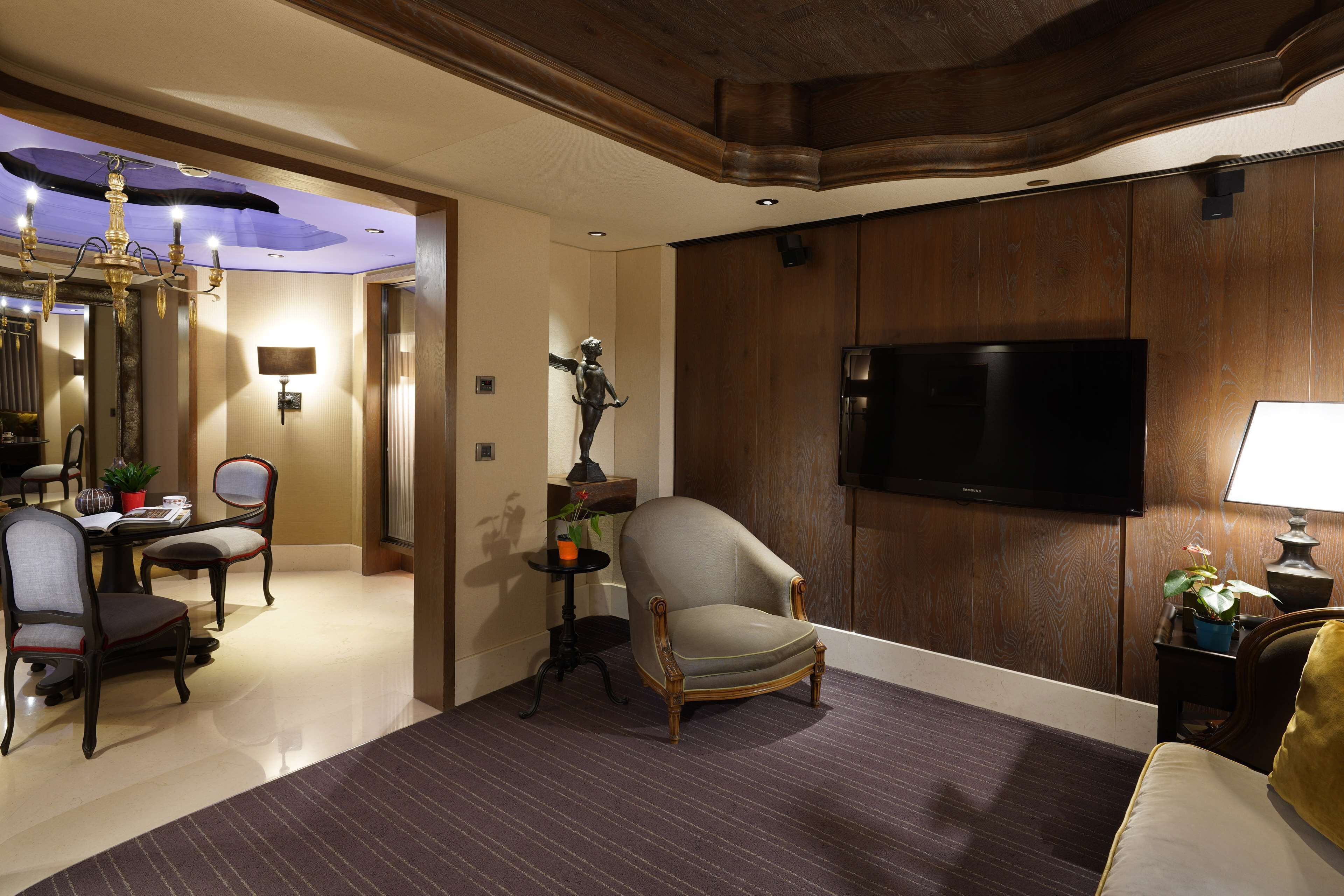 A hotel room with a flat-screen TV, a dining area with a chandelier, and a seating area with a sofa and armchairs.