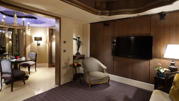 A hotel room with a flat-screen TV, a dining area with a chandelier, and a seating area with a sofa and armchairs.