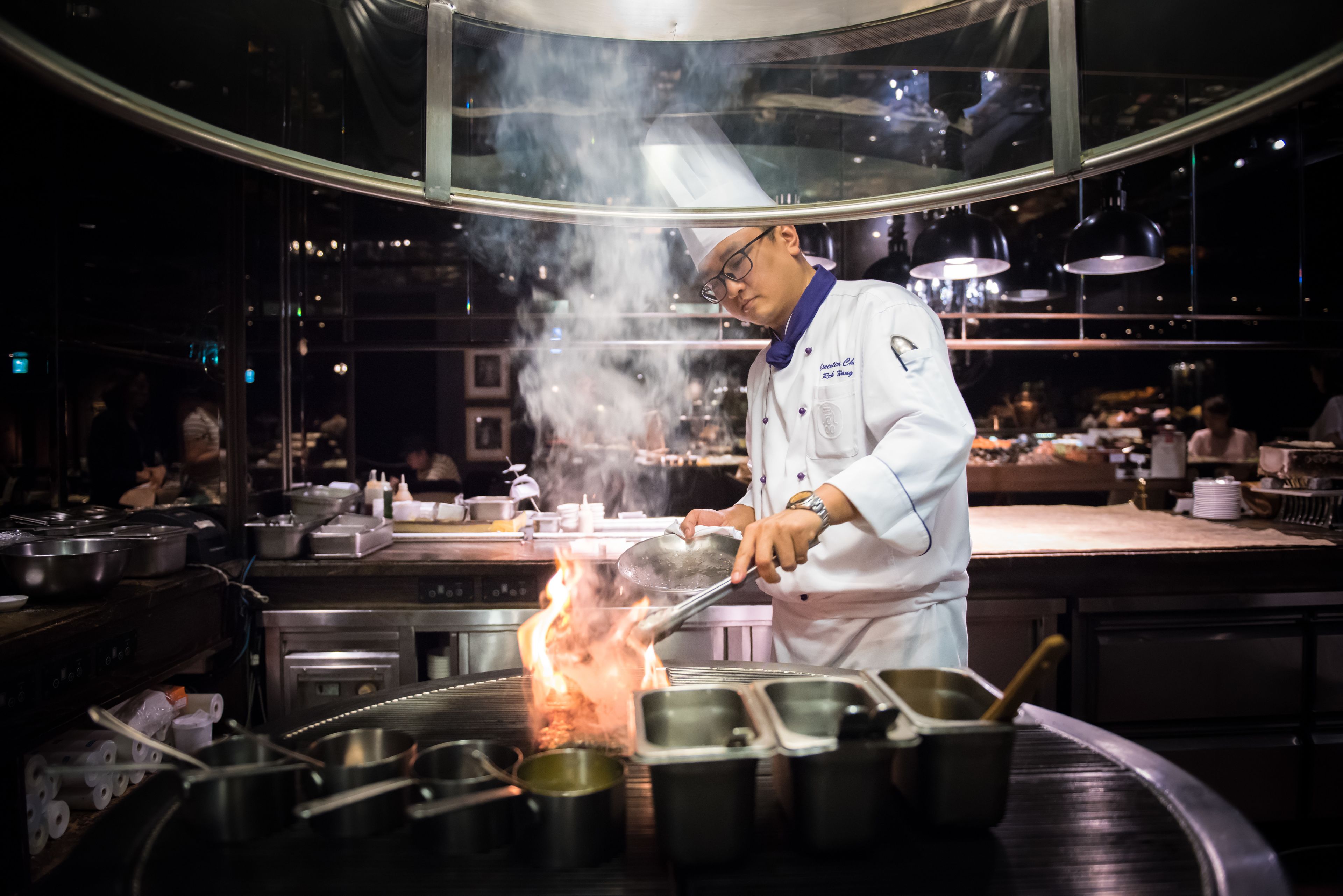A chef cooking with a large flame on a stove in a professional kitchen.