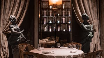 A dining area with a table set for two, surrounded by chairs, and two statues on either side.