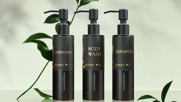 Drie zwarte flessen met de aanduidingen 'BODY CONDITIONER', 'BODY WASH' en 'SHAMPOO', met gouden tekst en een groene bladsymbool.