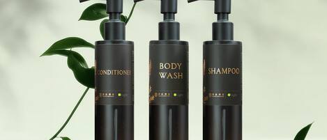 Three black bottles labeled "BODY CONDITIONER," "BODY WASH," and "SHAMPOO" with gold text and a green leaf symbol.